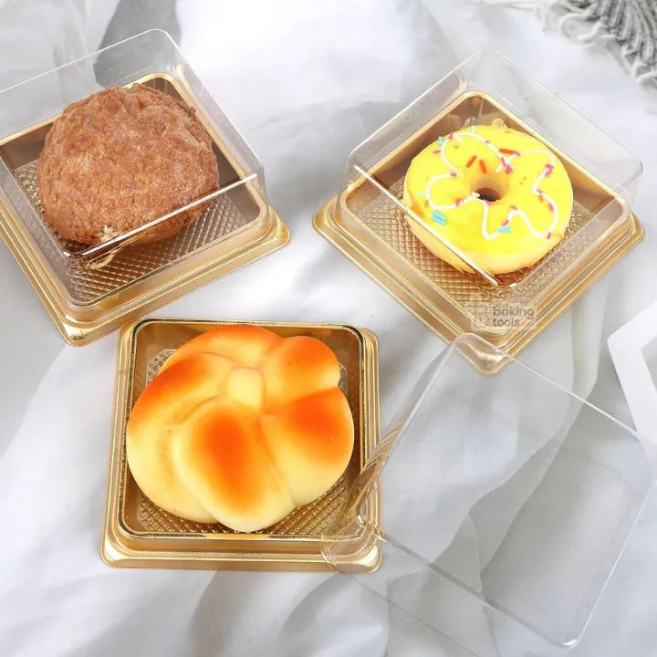 Three pastries in clear plastic containers on a white fabric background