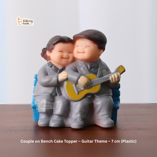 Couple on bench cake topper with guitar, sitting on a wooden surface.