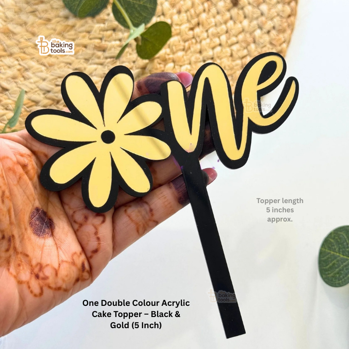Hand holding a double color acrylic cake topper with 'love' and a yellow flower design.
