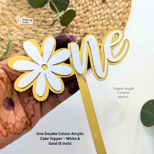 White and gold acrylic cake topper with a flower design held by a hand.