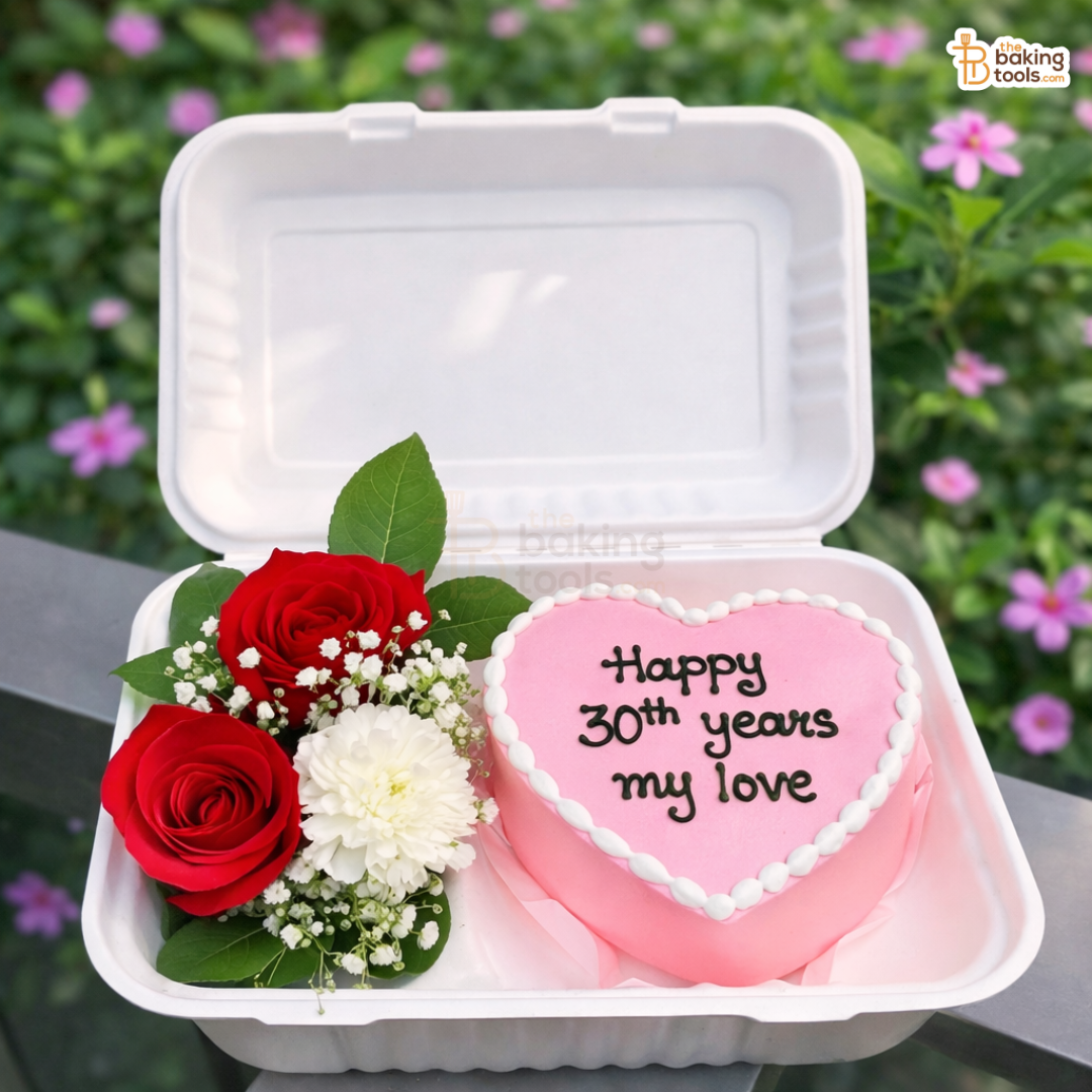 Heart-shaped cake with 'Happy 30th years my love' message and flower arrangement in a takeout container.