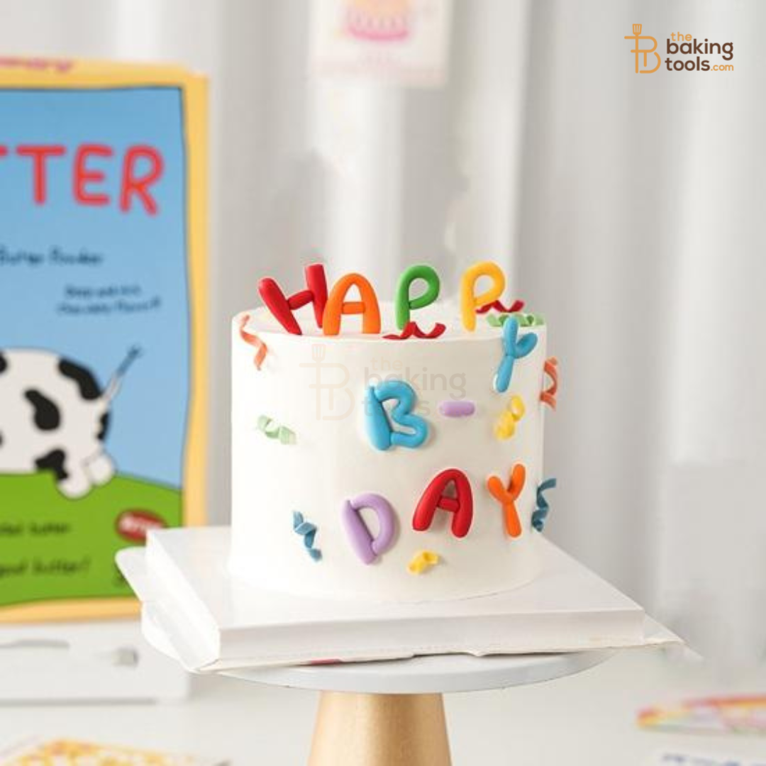 Small birthday cake with colorful 'HAPPY BIRTHDAY' letters on a stand, with a children's book in the background.