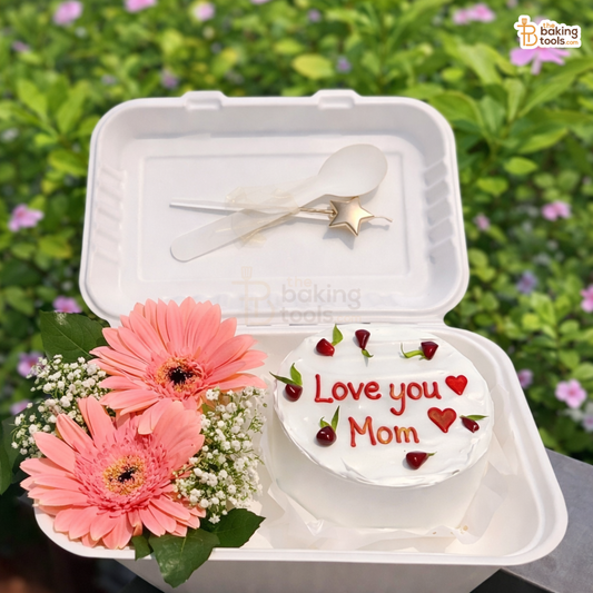 Small round cake with 'Love you Mom' message, pink flowers, and a spoon in a takeout container against a green background.